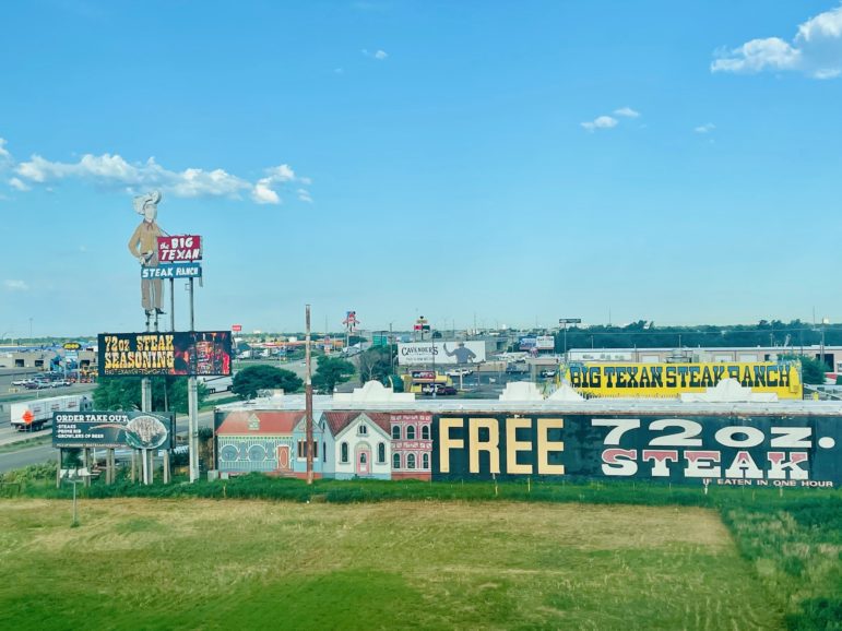 The side of a large building next to a highway is shown. "Free 72oz. steak" is printed on the side.