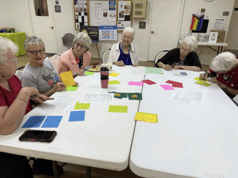 Sue, an educator and advocate for public education, organized a postcard writing party to direct messages to the SBOE. Here, 6 adults sit around tables writing on colorful postcards.